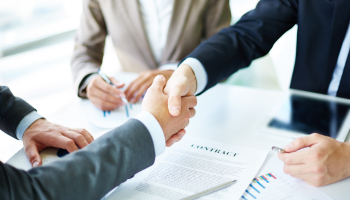 Two business individuals shaking hands above a stack of papers